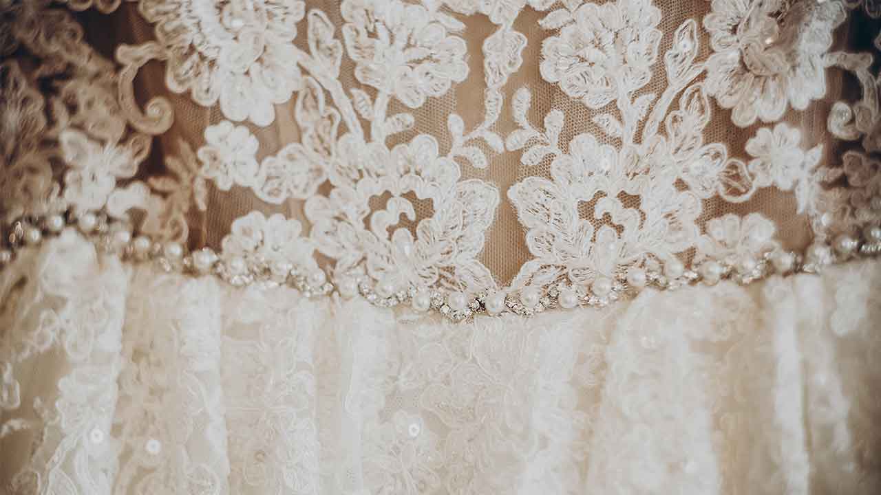 A close up of a wedding dress with lace and beading.