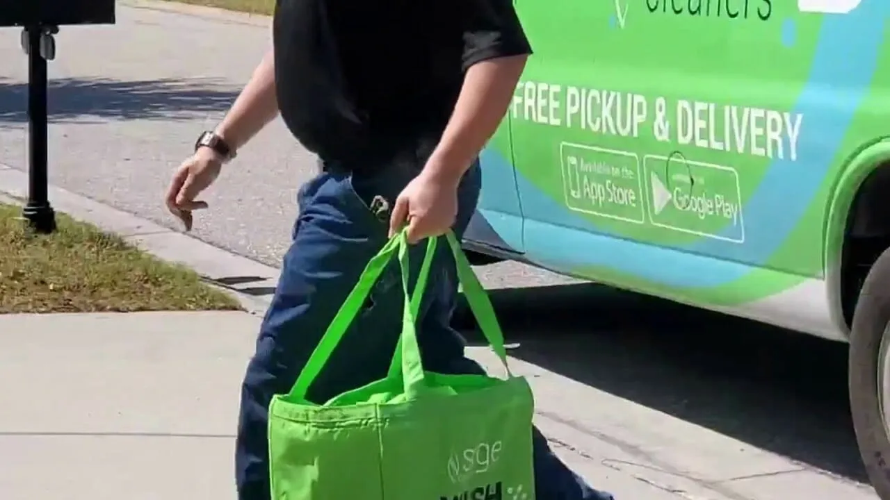 A man carrying a green bag walks down the sidewalk, possibly containing dry cleaning in St Petersburg.
