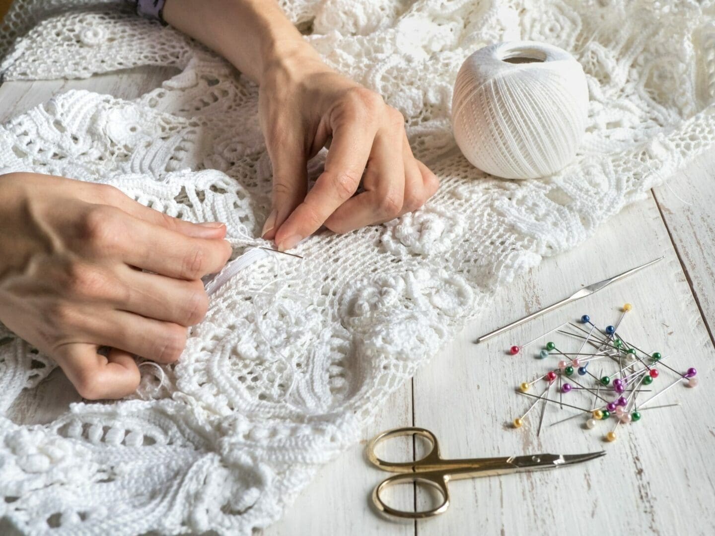 A woman's hands are working on a white crocheted blanket, while wondering how long dry cleaning a wedding dress takes.