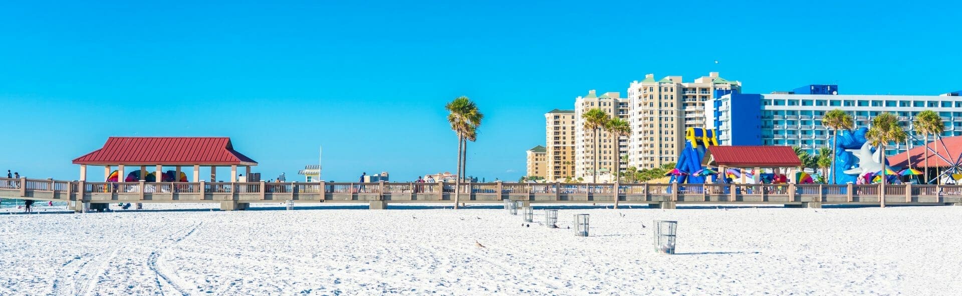 A white sand beach with palm trees and buildings.