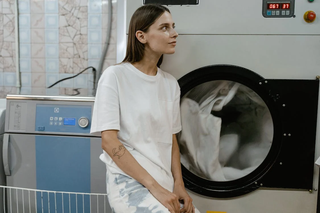 A woman sitting in front of a washing machine.