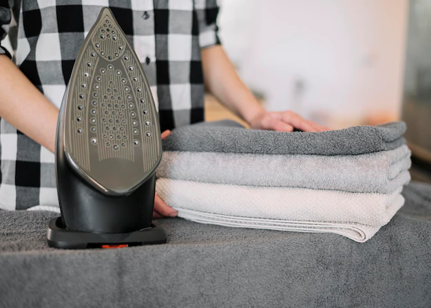 A woman ironing towels on a table.