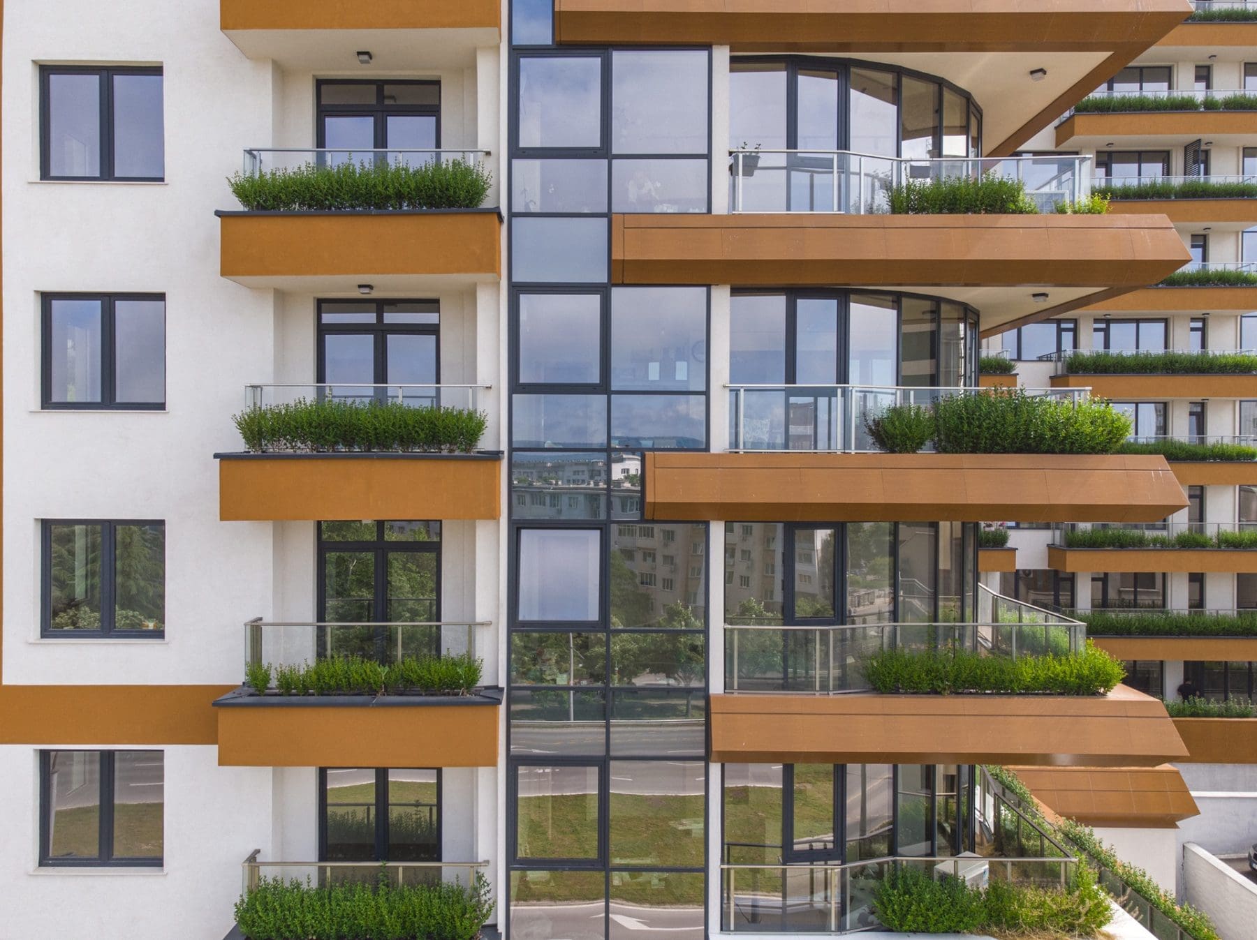Modern apartment building with large glass windows, orange balconies, and green plants lining the balcony railings.