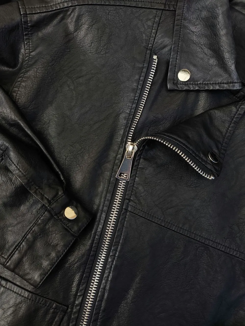 Close-up of a black leather jacket featuring a silver zipper, snap buttons, and visible stitching details.